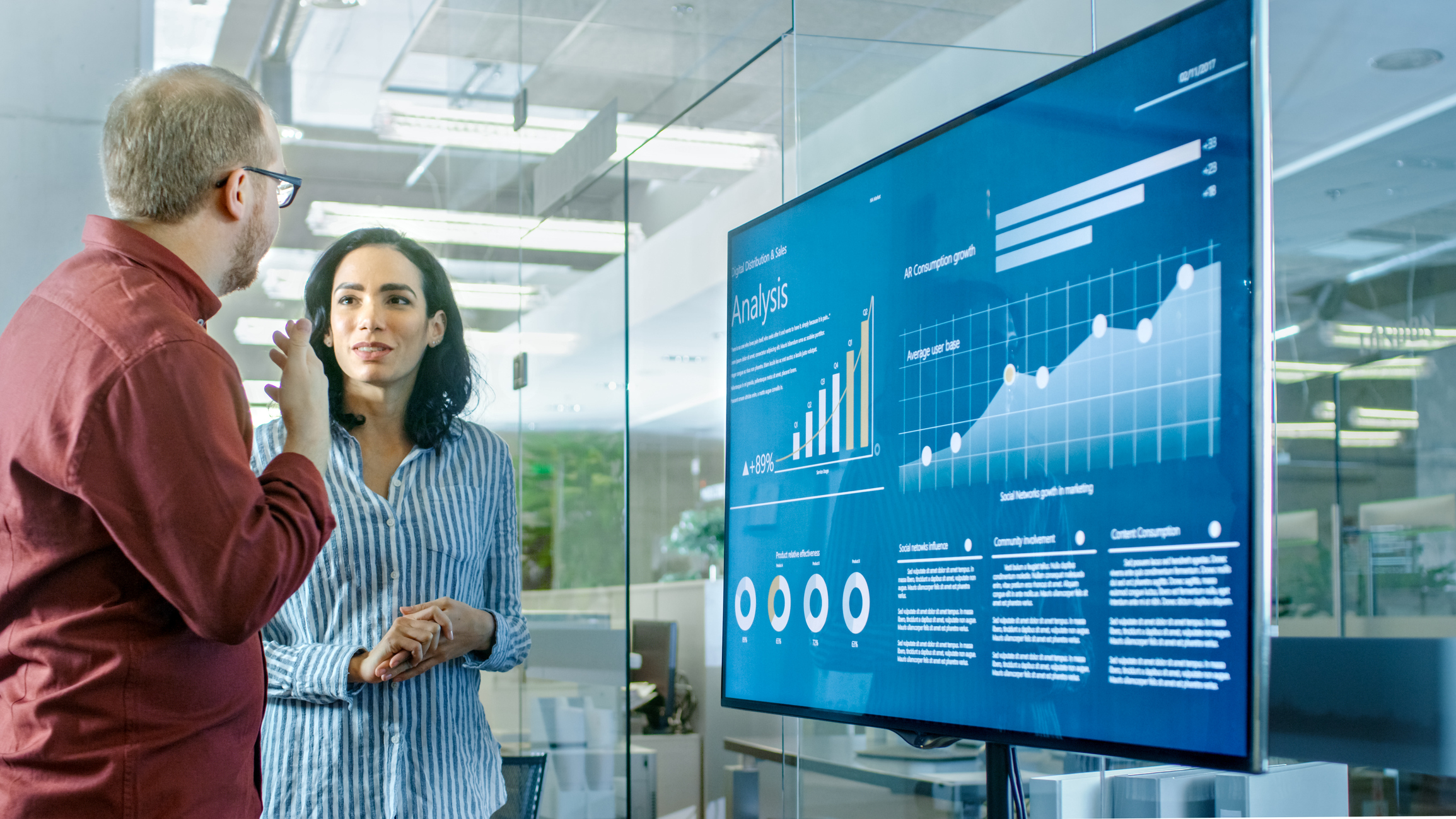 Two people discussing in front of a large monitor with boxes for Ethics, Oversight , Transparency shown on the screen