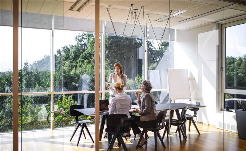 In an office, two people calculating water footprint metrics, with green landscapes visible through the window.