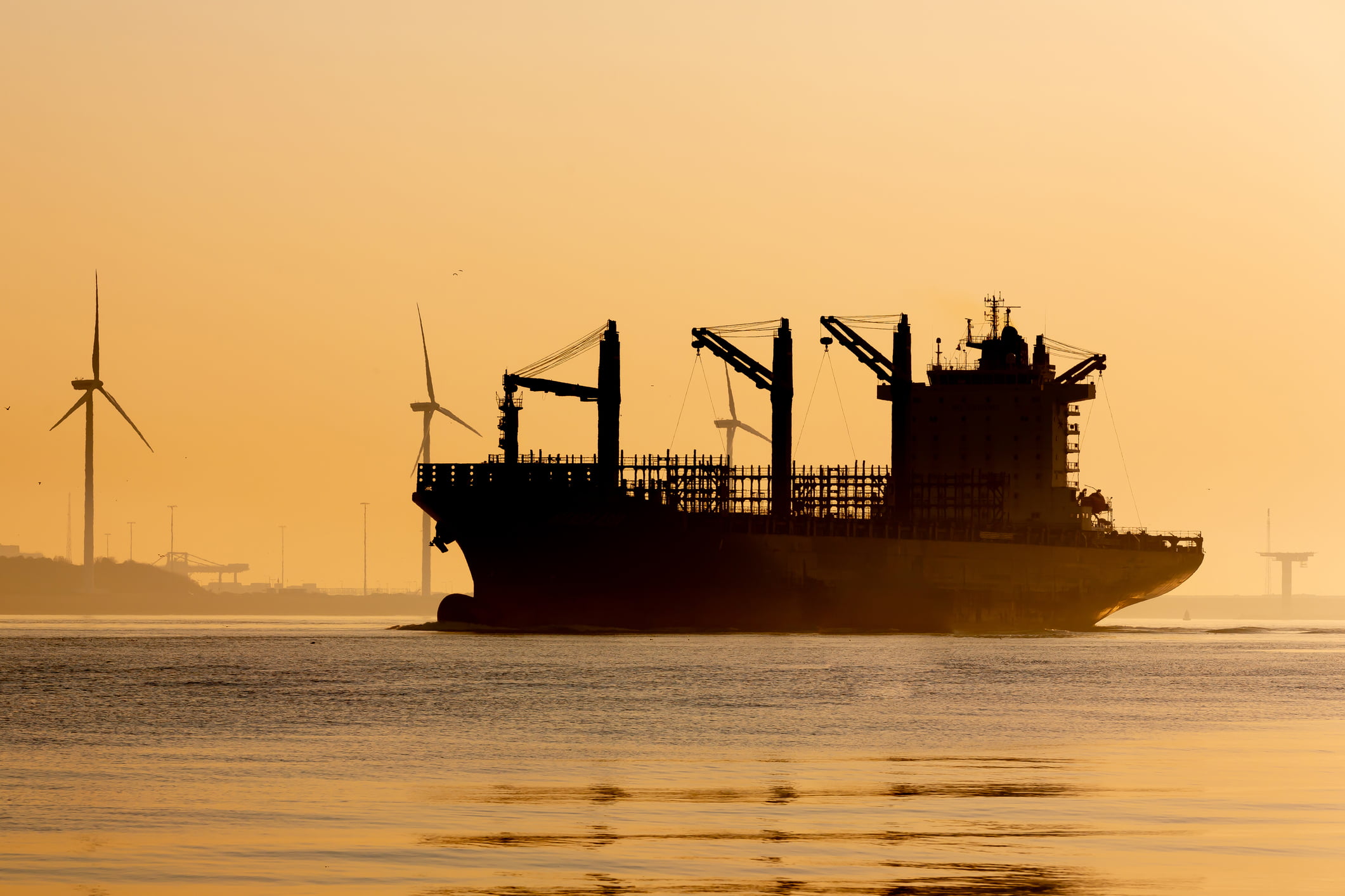 Silhouette of a large freight ship and wind turbines at sunset