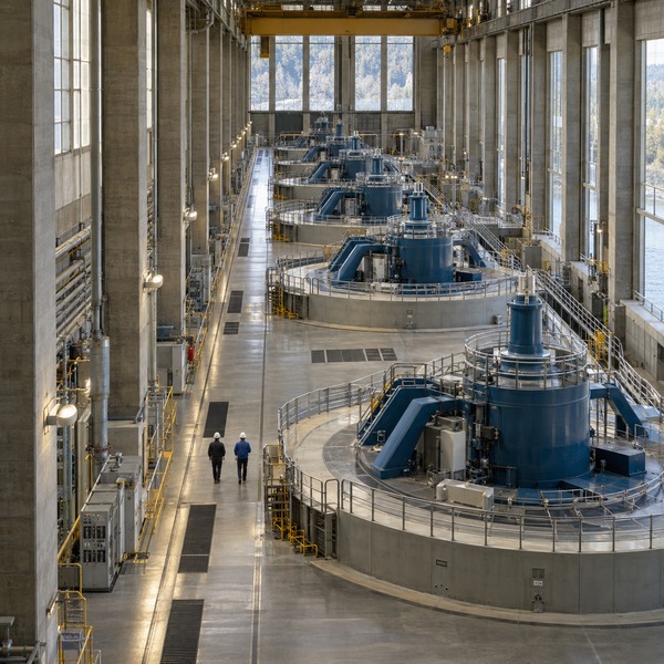 Engineers walk through a hydroelectric turbine hall with repeating generator units extending across the facility.