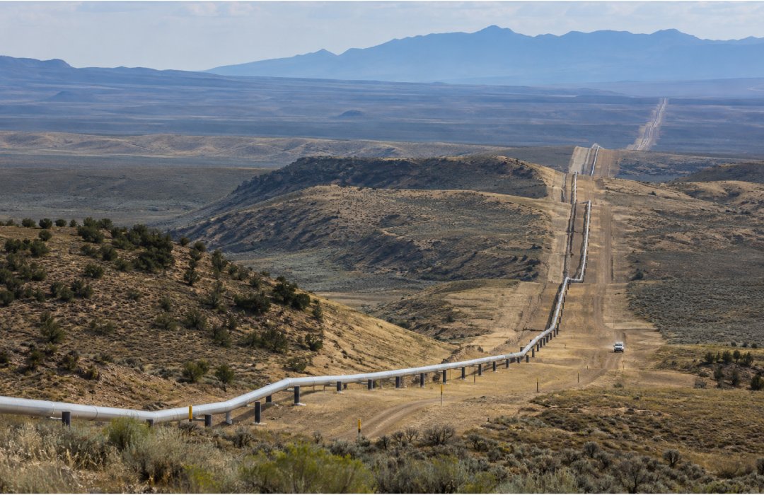 Gas pipeline and right-of-way extending across a vast semi-arid landscape toward distant mountains.