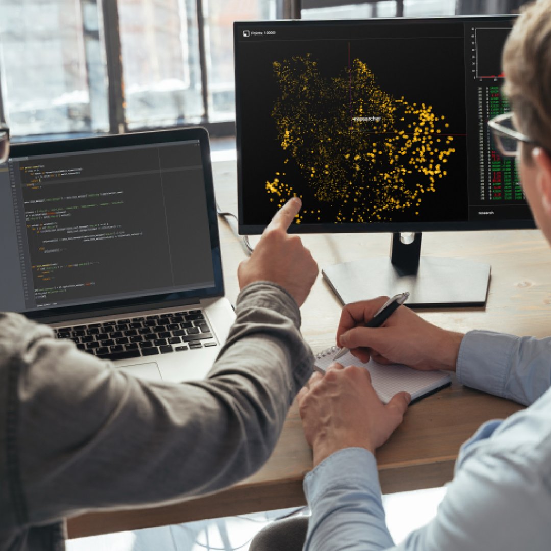 Two technology specialists reviewing code and a complex data visualization on connected screens during an analytical modelling session.