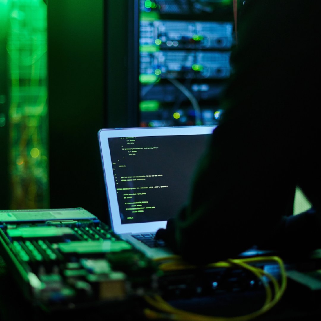 Technology specialist working on a laptop beside server racks in a secure data center environment.